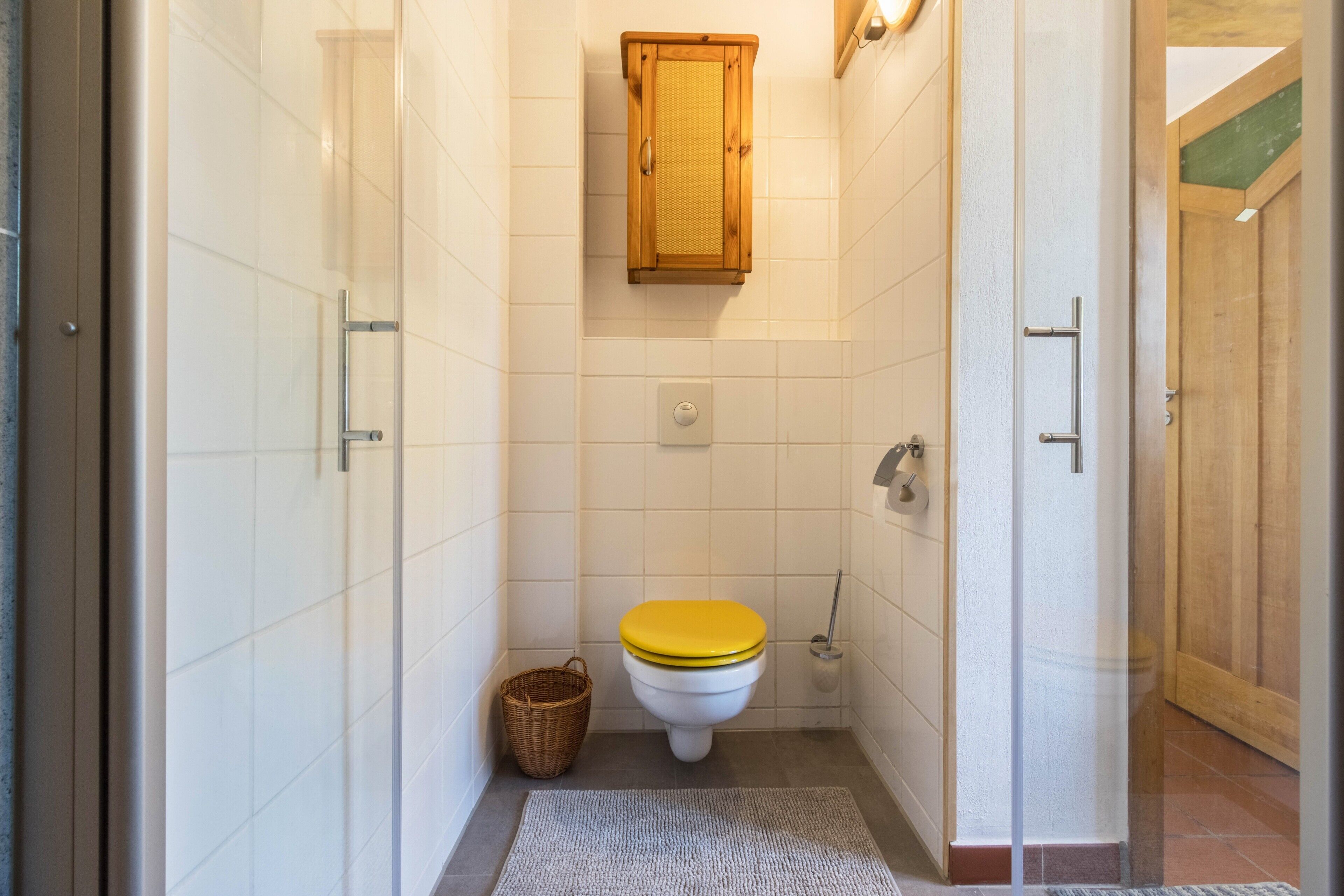 Ein kleines Badezimmer mit Toilette, einem Holzschrank und Fliesenboden.
