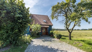 Une maison avec une allée pavée menant à une porte en bois, entourée de verdure et sous un ciel dégagé.