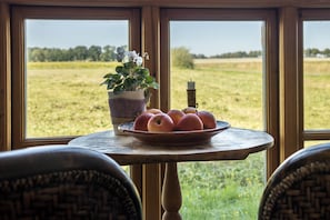A table with a bowl of fruit and a potted plant by a window with a view of a field.