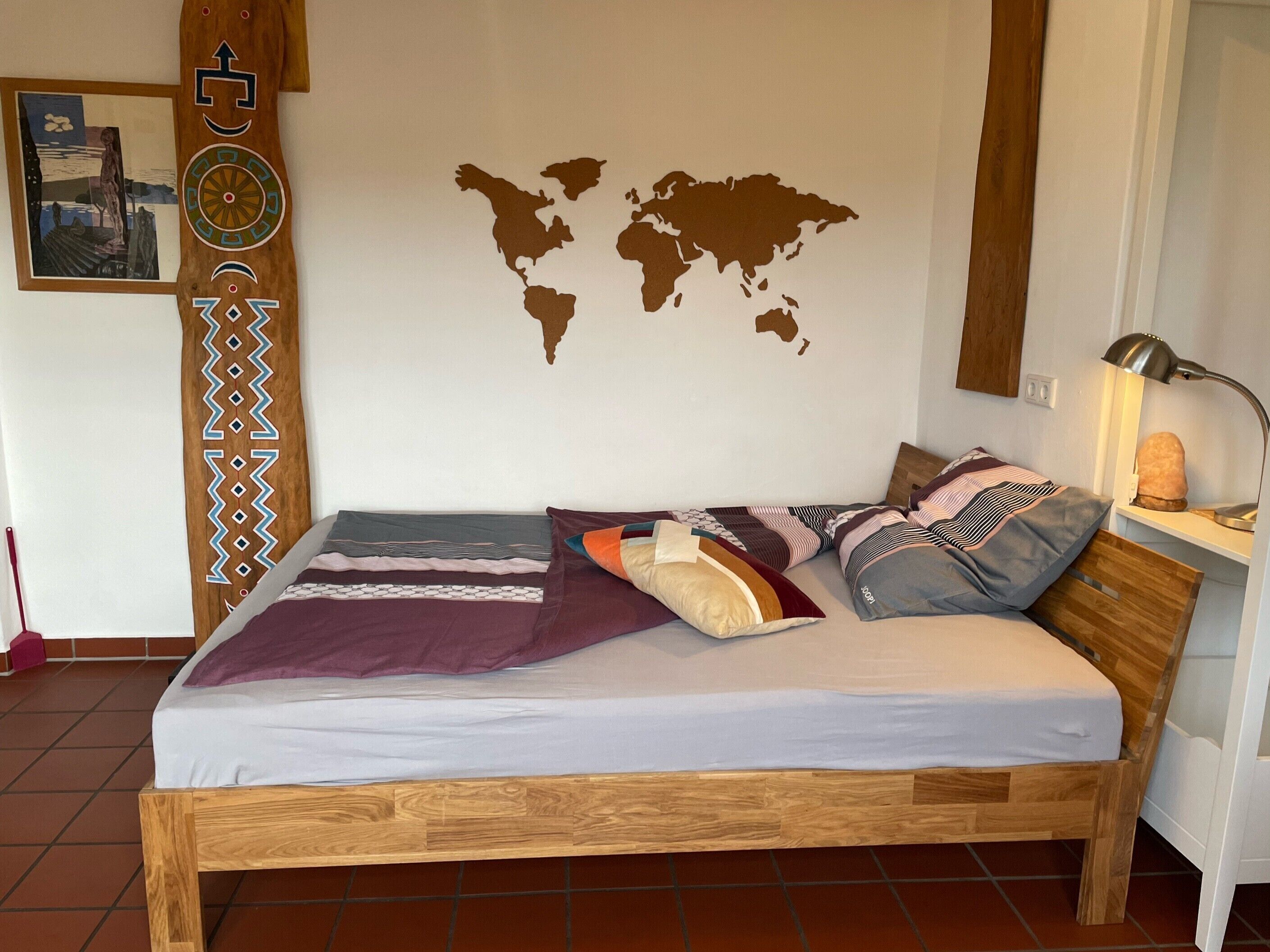A bed with a wooden frame, a world map on the wall, a lamp, and a picture of a landscape.