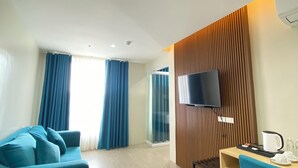 Ein modernes Hotelzimmer mit einem Türkis-farbenen Sofa, einer Wandverkleidung aus Holz, einem Flachbildfernseher und einem Essbereich mit Kaffeemaschine.