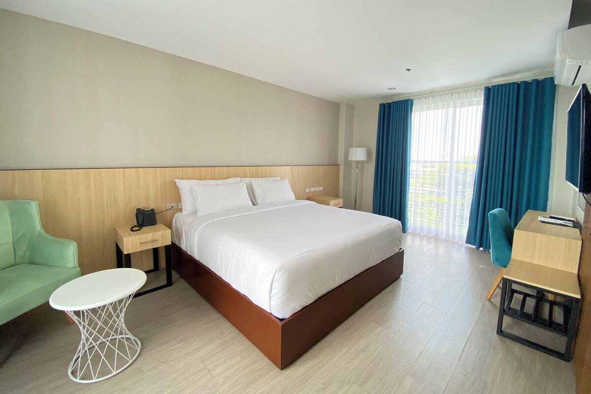 A hotel room with a large bed, a desk with a chair, a small table, a phone on the nightstand, and a TV on the wall.