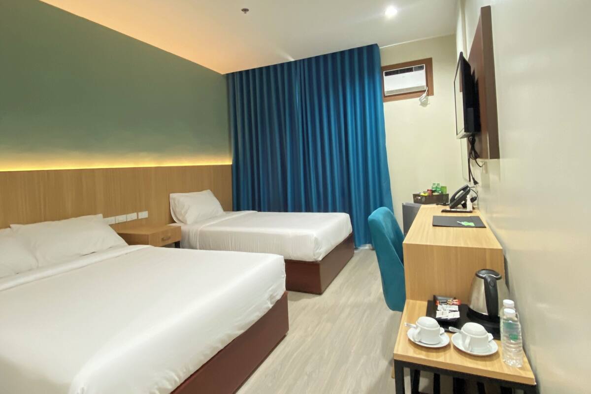 A hotel room with two beds, a desk, a chair, a coffee maker, and a TV.