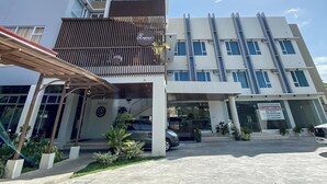 Ein mehrstöckiges Hotel mit modernem Design, das eine markante Eingangspforte mit überdachtem Gang und einen Parkplatz davor aufweist.