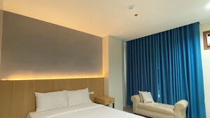Ein modernes Hotelzimmer mit einem großen Bett, einer Couch, einem Nachttisch und einem Fenster mit blauen Vorhängen.