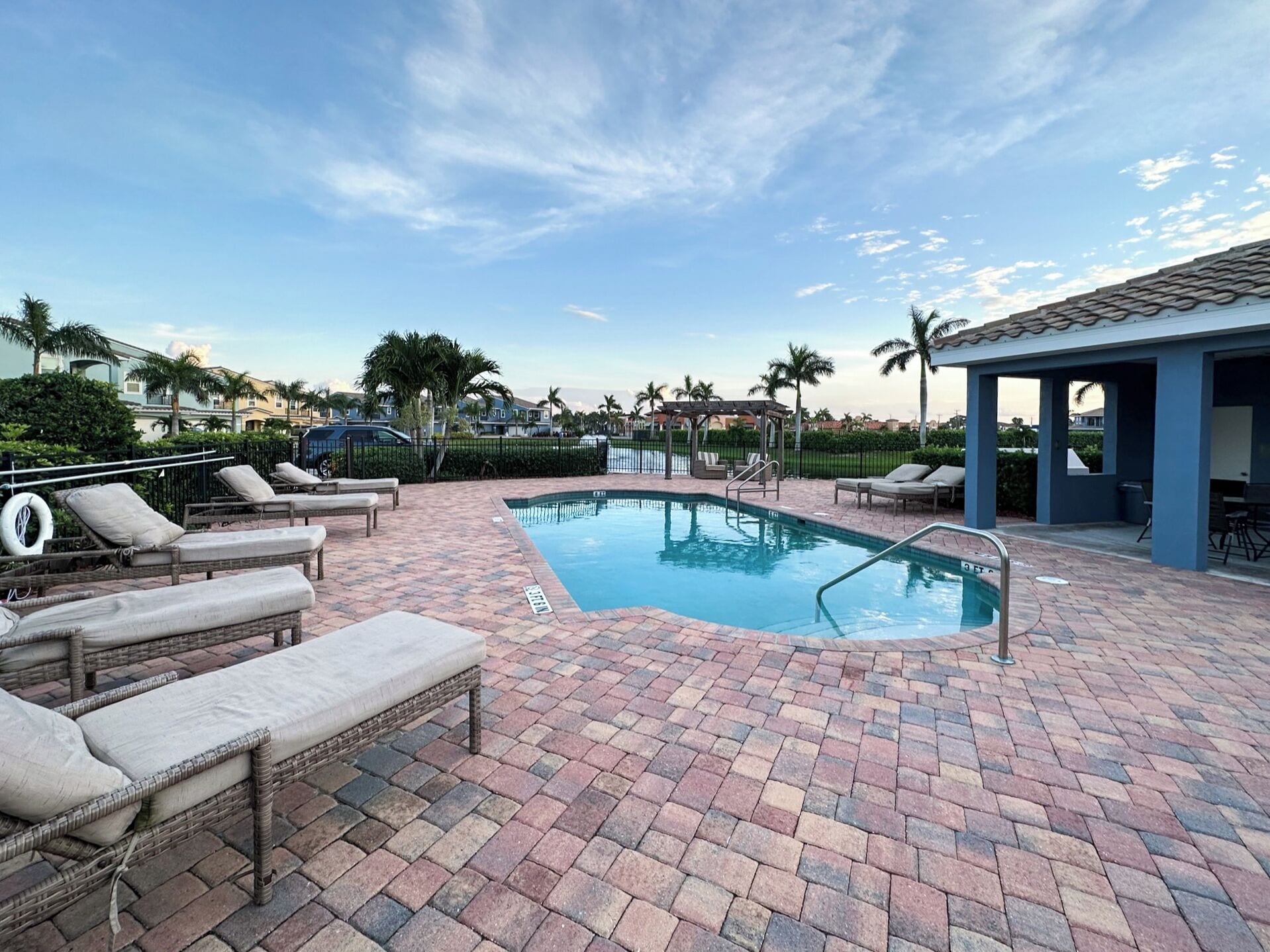 A rectangular swimming pool with a tiled deck, surrounded by lounge chairs and a covered seating area.