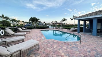 A rectangular swimming pool with a tiled deck, surrounded by lounge chairs and a covered seating area.