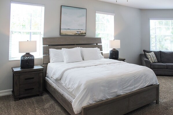 A bedroom with a bed, nightstands, a lamp, a painting, and a sofa.
