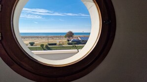 A round window with a clear view of a beach and a building with solar panels. - Cozy Studio With Side sea View in Bibione (San Michele al Tagliamento)