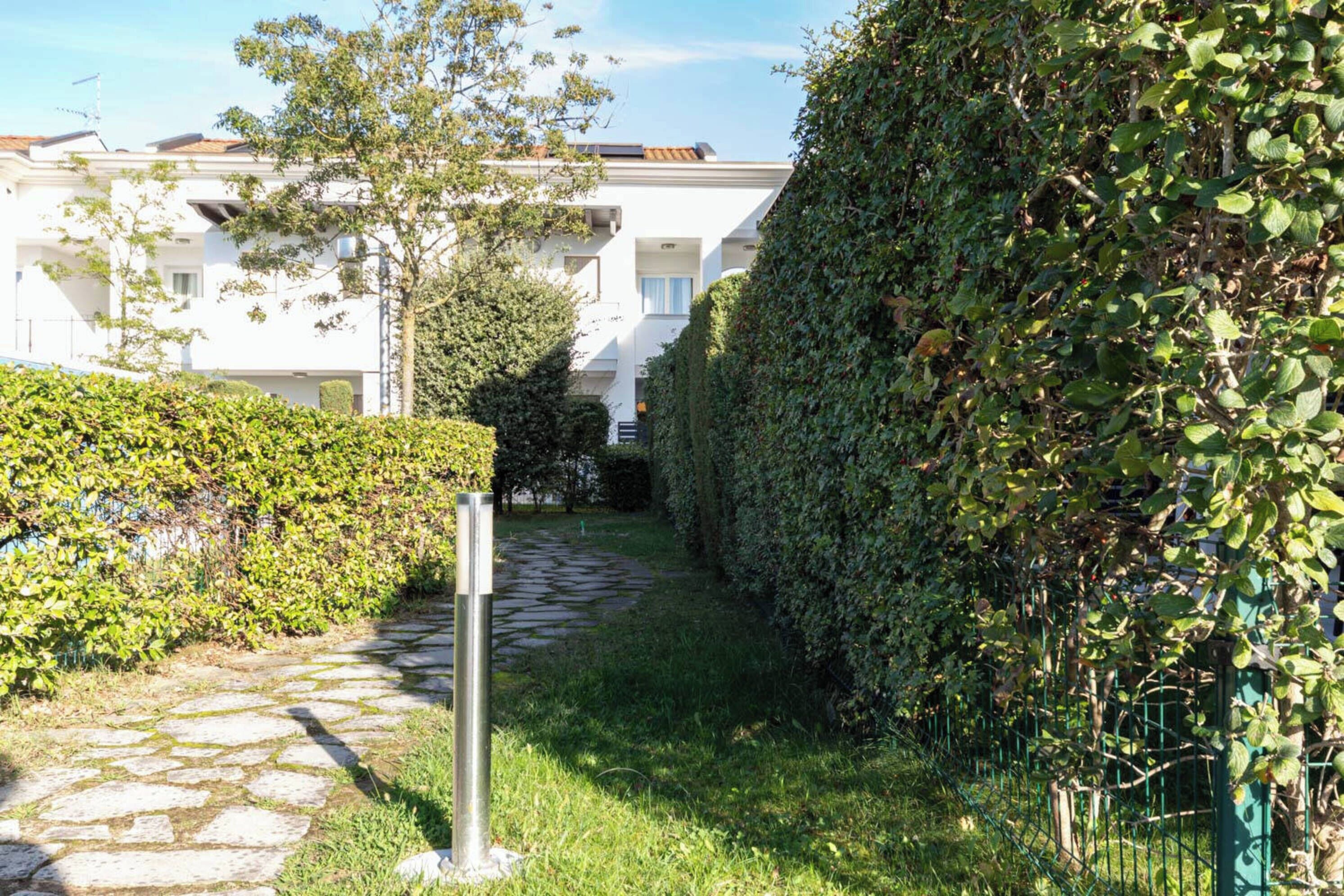 A pathway leading to a building with a white facade, surrounded by lush greenery and a stone path.