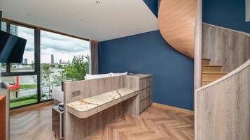 A modern interior with a herringbone wooden floor, a curved wooden staircase, and a view of a cityscape through large windows.
