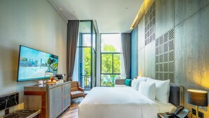 A modern hotel room with a large bed, a desk with a chair, a television, and a view of greenery through large windows. - Ten Six Hundred, Chao Phraya, Bangkok by Preference, managed by The Ascott Limited (Bangkok)