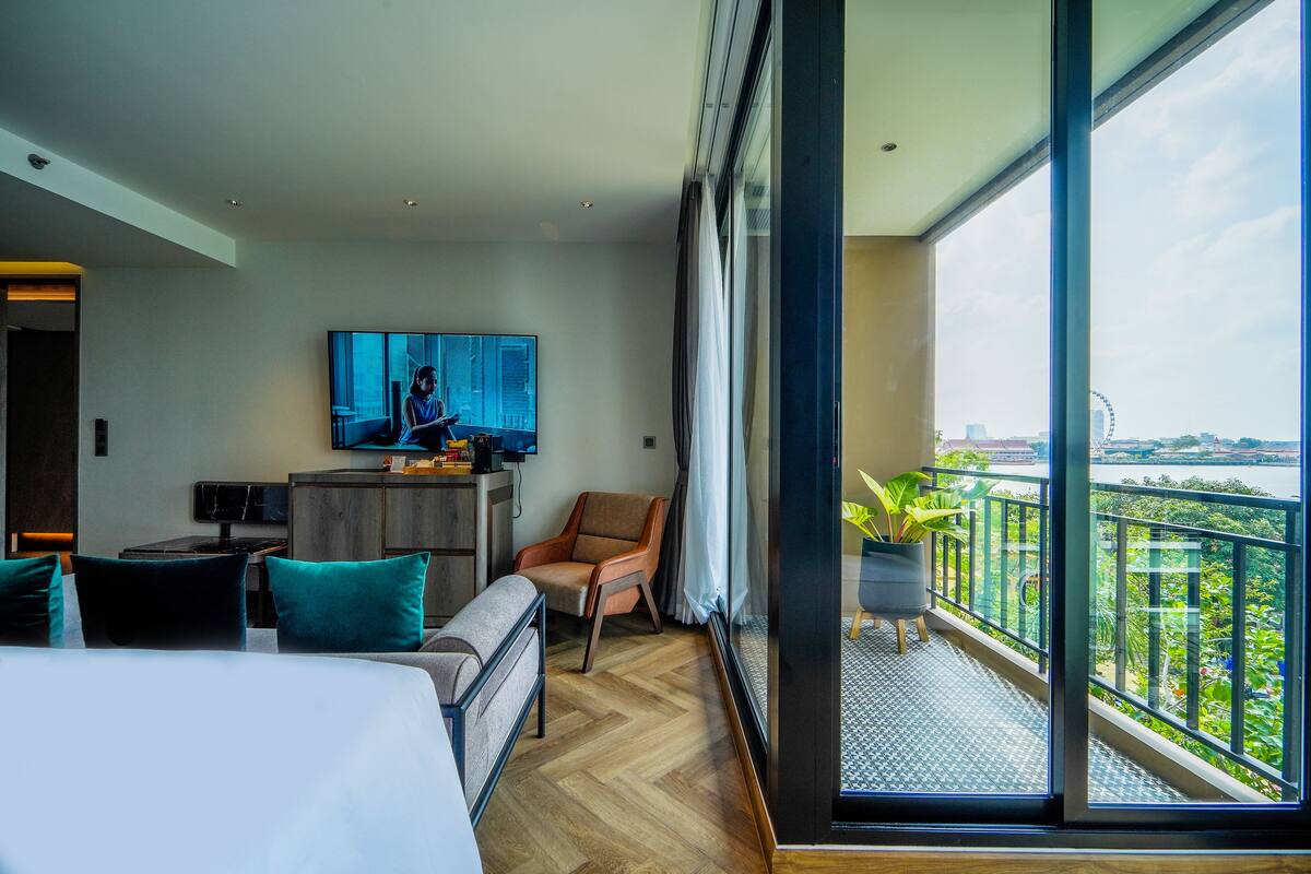 Ein modernes Hotelzimmer mit einem großen Bett, einer Sitzecke mit Sofa und Sesseln, einem an der Wand befestigten Fernseher und einem Balkon mit Blick auf die Stadt.