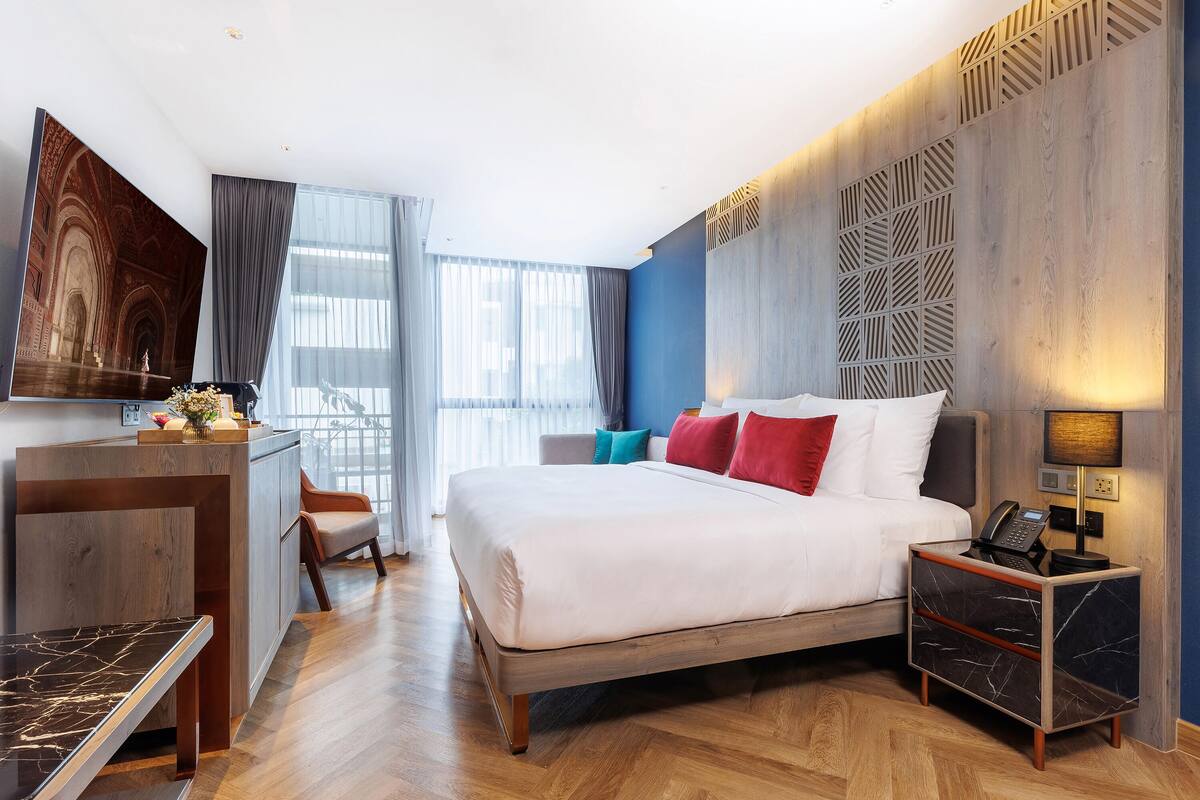 Ein modernes Hotelzimmer mit einem großen Bett, einem Schreibtisch, einem Sessel und einem Nachttisch mit einer Lampe.