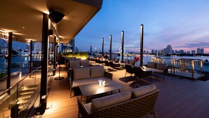 An outdoor terrace with seating, a view of the city skyline, and a waterfront. - Ten Six Hundred, Chao Phraya, Bangkok by Preference, managed by The Ascott Limited (Bangkok)