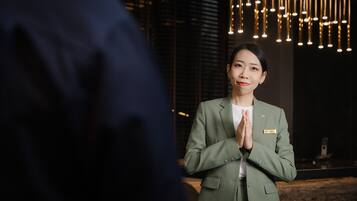 A person in a green suit with a name tag, standing in a room with a modern chandelier and a wooden floor.