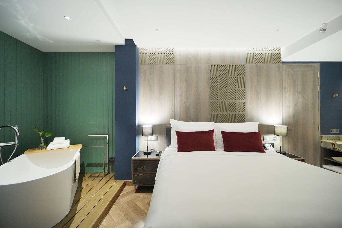 Ein modernes Hotelzimmer mit einem großen Bett, Holzboden, einer Badewanne und einem kleinen Schreibtisch.