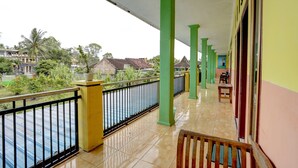 A balcony with green pillars, a tiled floor, and a view of houses and trees in the background. - Hotel O Anisah Adil Homestay SyariahNearsmart Kampung Desa Pakistaji (Banyuwangi)