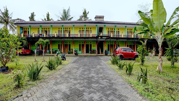 A two-story building with a paved entrance, surrounded by greenery and parked vehicles. - Hotel O Anisah Adil Homestay SyariahNearsmart Kampung Desa Pakistaji (Banyuwangi)