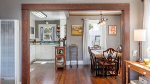 Un coin repas avec une table et des chaises en bois, une cuisine en arrière-plan et une vue sur l’extérieur.