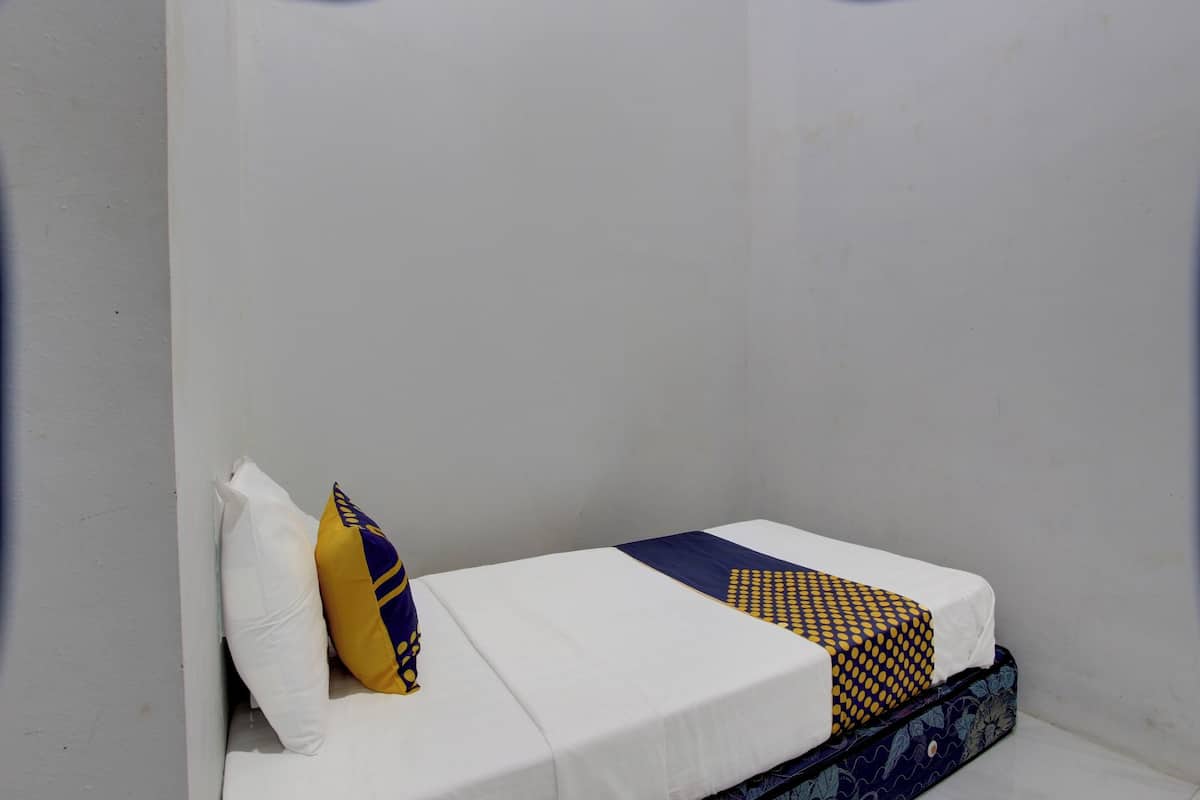 Een enkel bed met een witte matras, een deken met blauw en geel patroon, en een wit kussen.