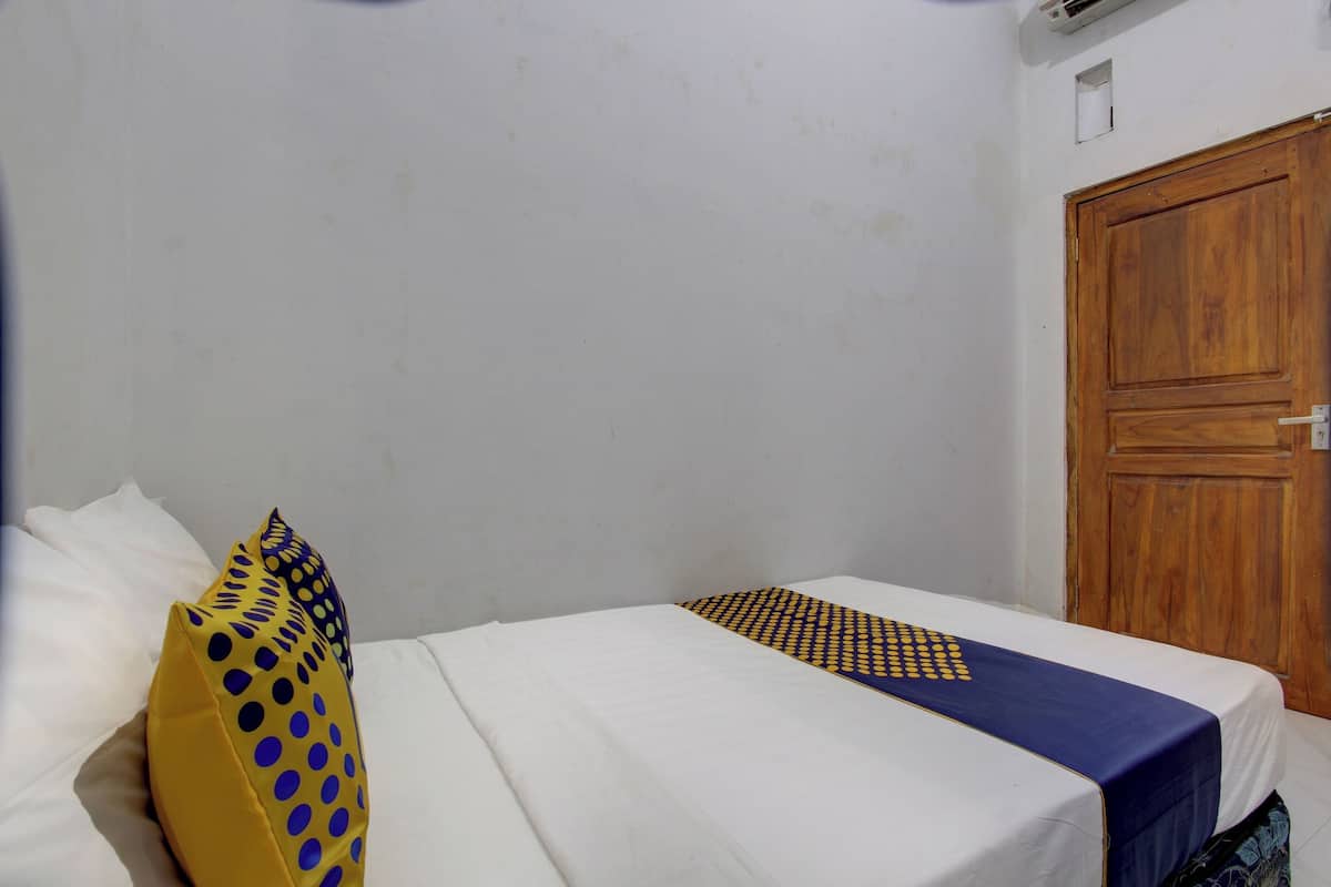 Een eenpersoonsbed met wit beddengoed, een kussen met blauw-geel patroon en een blauw-gele sprei.