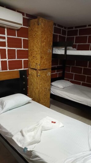 Une chambre de dortoir avec des lits superposés, une armoire en bois et un appareil de climatisation fixé au mur.