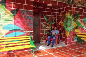 Un homme est assis sur un banc rouge devant un bâtiment dont les murs sont décorés de peintures murales colorées.