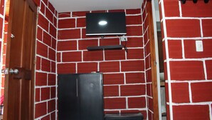 Une pièce aux murs en briques rouges, avec un meuble noir, un téléviseur à écran plat fixé au mur et une porte en bois.