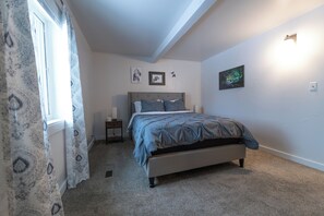 A bedroom with a bed, a nightstand, a window with patterned curtains, and wall-mounted artwork. - Centrally Located, comfortable 2 bedroom home (Fairbanks)