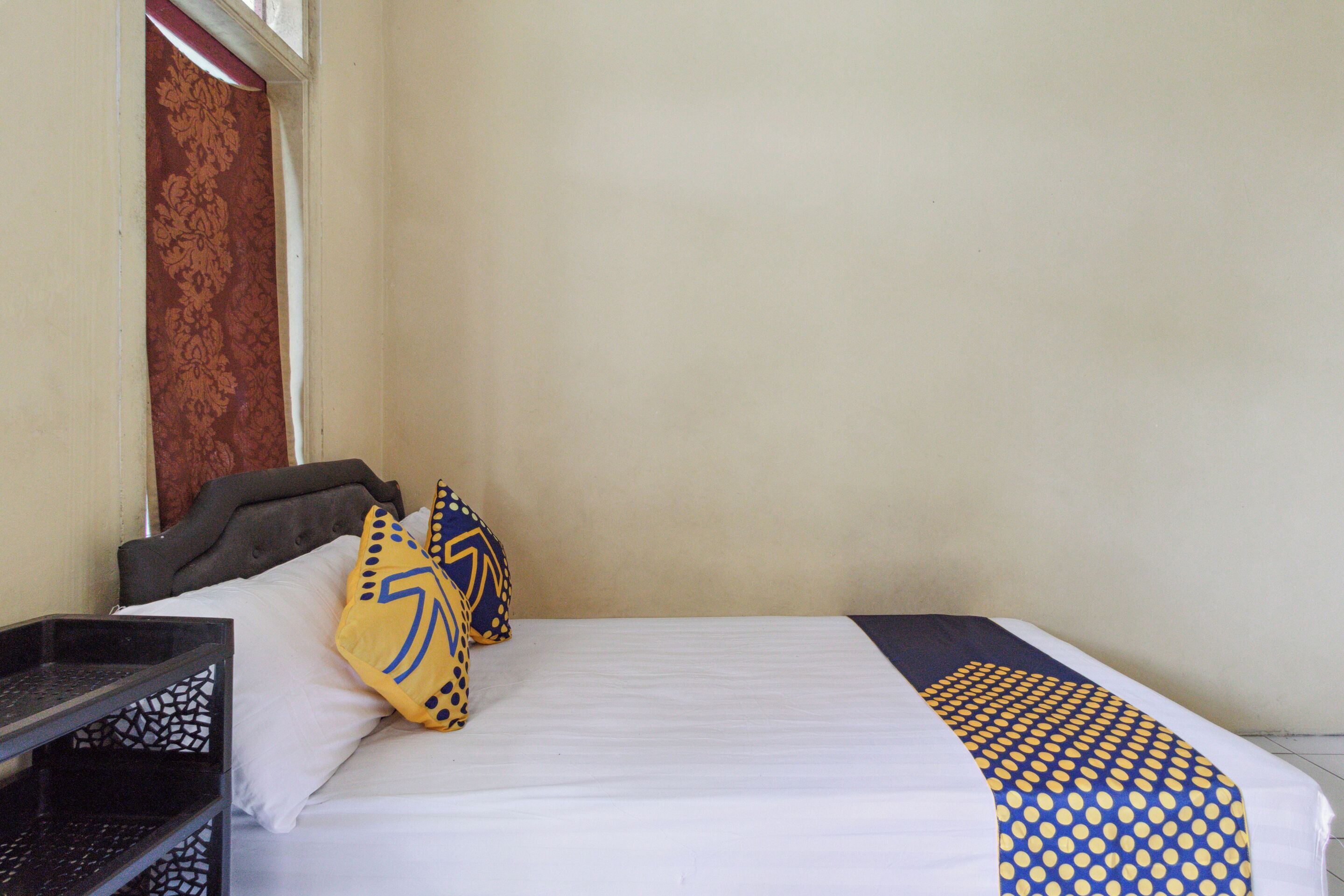 A hotel room with a bed, pillows, a nightstand, and a window.