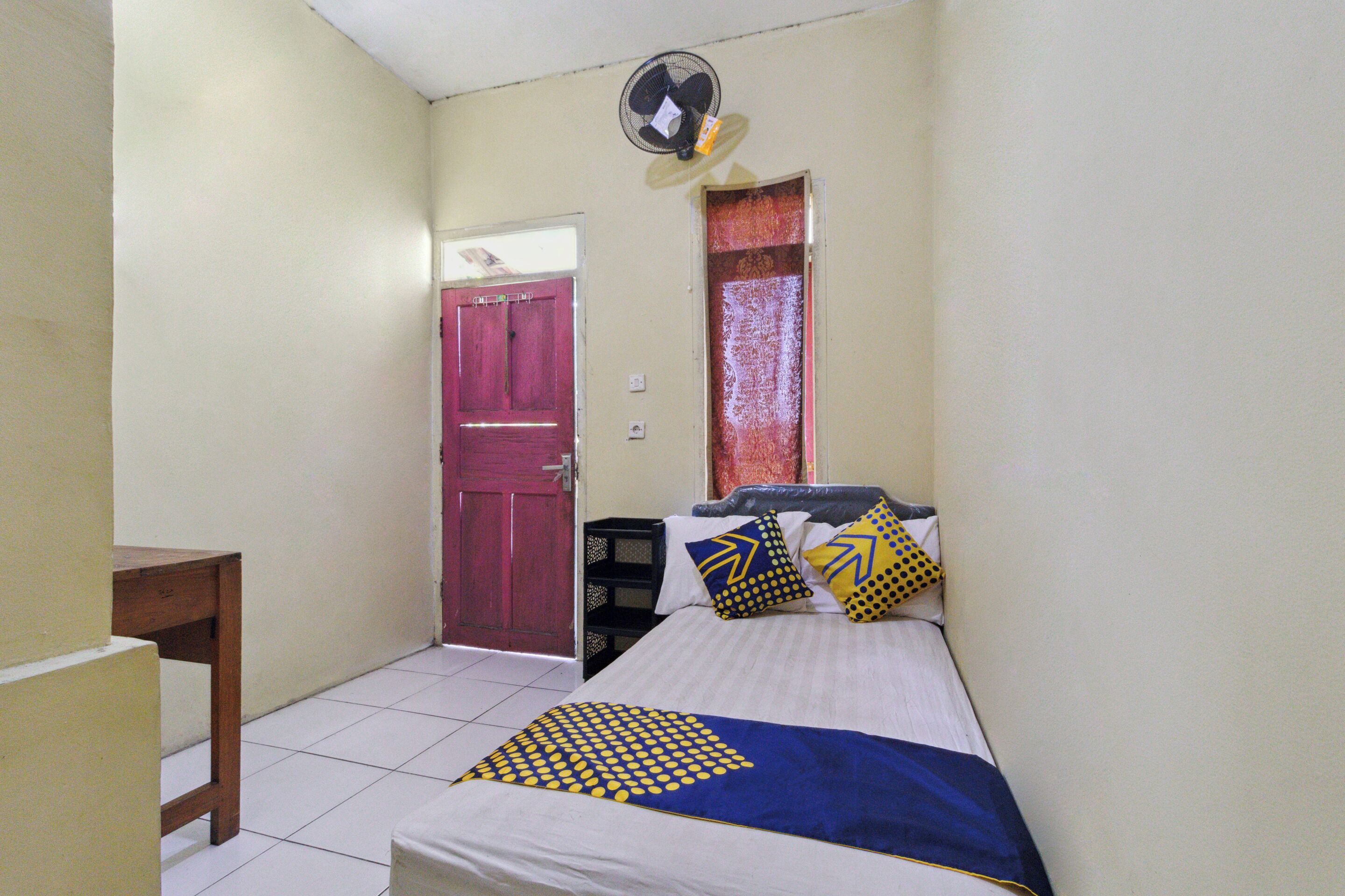 A small, neatly arranged bedroom with a bed, a desk, and a door.