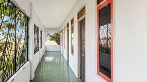 Un pasillo con piso verde estampado, paredes blancas y ventanas con marcos rojos.