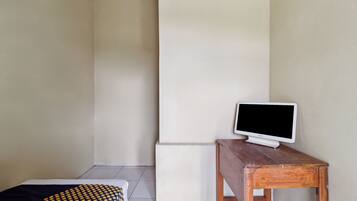 A room with a bed, a wooden table with a television, and a white pillar.
