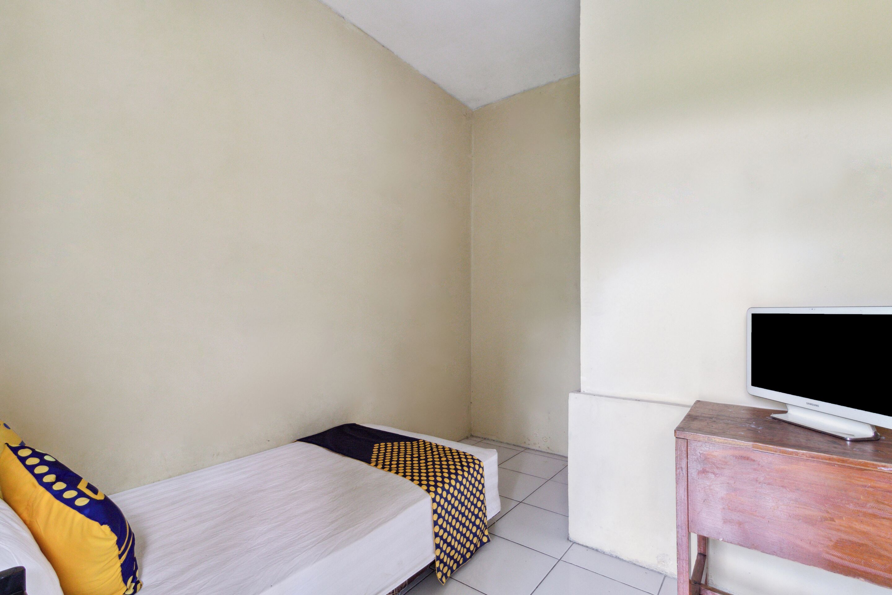 A small, clean room with a bed, a TV on a wooden stand, and a white wall.