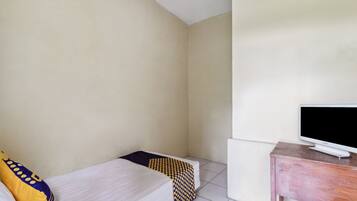 A small, clean room with a bed, a TV on a wooden stand, and a white wall.