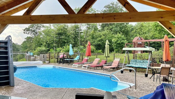 A covered outdoor swimming pool with lounge chairs and umbrellas, surrounded by a wooden deck and a fence. - Family & pet-friendly, peaceful rural escape. Hiking nearby. (Harding)