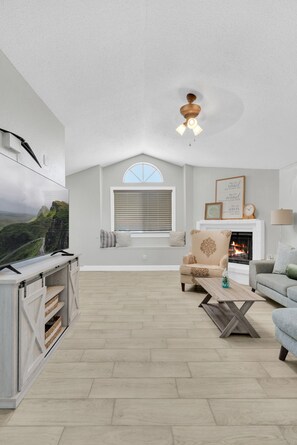 A spacious living room with a fireplace, a mounted TV, and a ceiling fan.