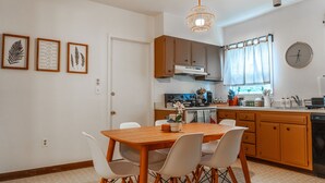 Une cuisine avec des meubles de rangement en bois, une table à manger avec des chaises, un luminaire suspendu et une horloge au mur.