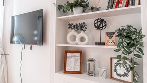 Une étagère blanche avec des livres, un panneau d’accueil encadré, des vases décoratifs, une plante en pot et un chandelier.