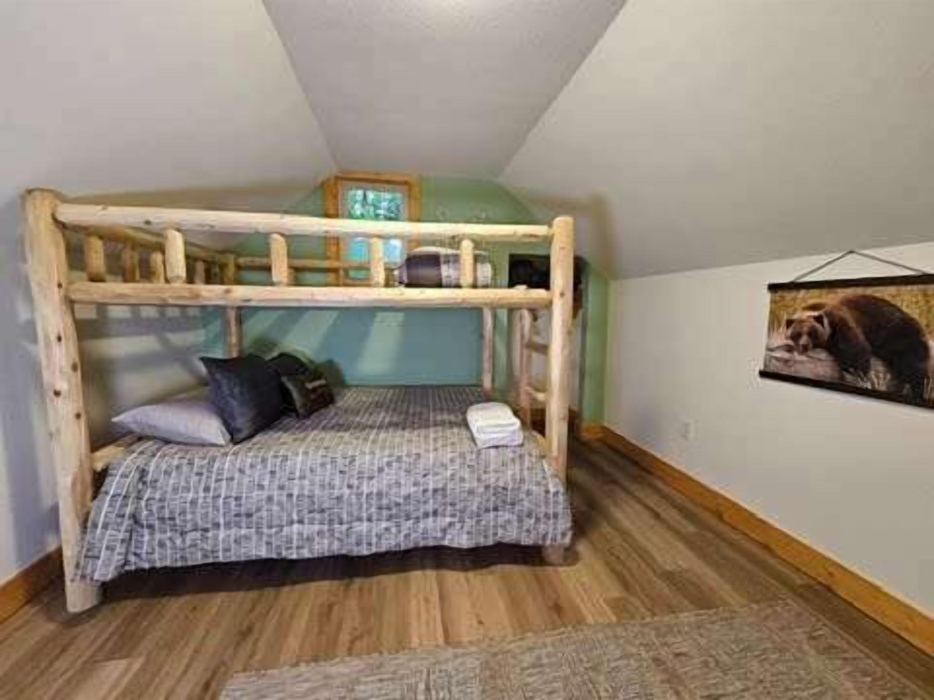 A bunk bed with a wooden frame, a patterned bedspread, and a framed picture on the wall.