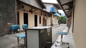 A covered outdoor seating area with a table and chairs, a water dispenser, and a brick wall. - Hotel O Penginapan Raja (Sukabumi)