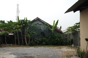 A house with a sloped roof, surrounded by banana trees and potted plants. - Hotel O Penginapan Raja (Sukabumi)