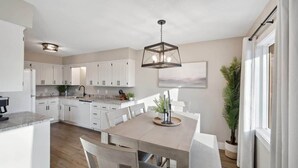 Une cuisine moderne avec des meubles blancs, un îlot central et un luminaire suspendu.