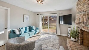 Un salon avec un canapé bleu, un tapis à motifs, une cheminée et un téléviseur fixé au mur.