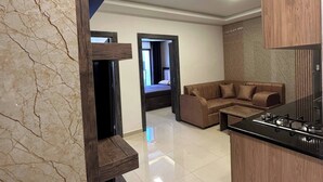 A modern kitchen with a black countertop and wooden cabinets, a brown leather sofa, and a tiled floor.
