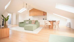 A spacious loft apartment with a high ceiling, a green sofa, a dining area, and a kitchen.
