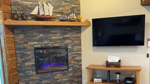 Una sala de estar con chimenea de piedra, un televisor de pantalla plana en la pared, una mesa de centro de madera y una alfombra estampada.