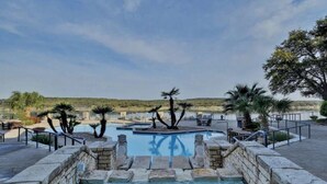 A pool area with stone steps leading into a hot tub, surrounded by palm trees and a view of the landscape. - Luxury Condo on Lake Travis with Scenic Views, 3 Pools, Hot Tub, Gym, Tennis, Sauna, Pickleball (Lago Vista)