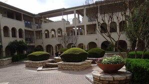 A courtyard with a brick-paved ground, surrounded by a multi-story building with arched windows and balconies. - Luxury Condo on Lake Travis with Scenic Views, 3 Pools, Hot Tub, Gym, Tennis, Sauna, Pickleball (Lago Vista)